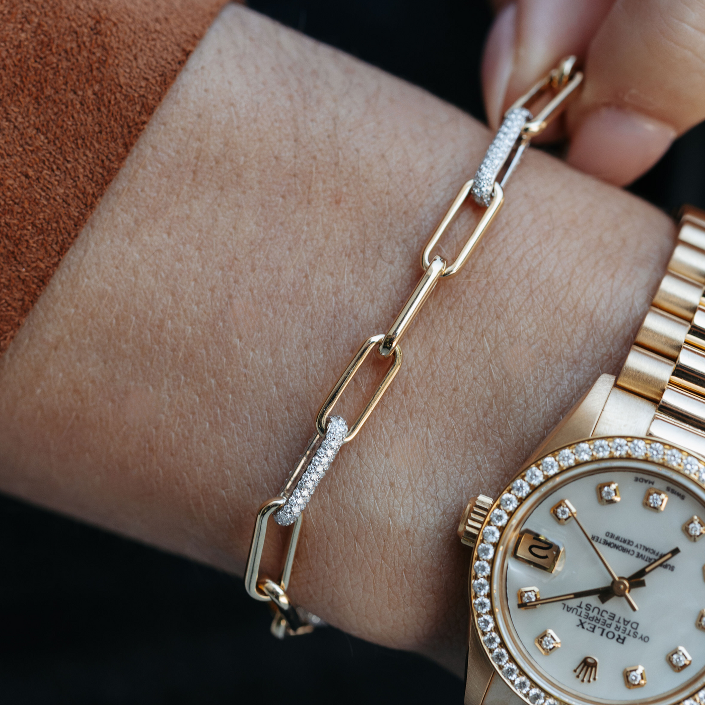 a woman wearing a diamond and gold paperclip link bracelet with a gold rolex watch